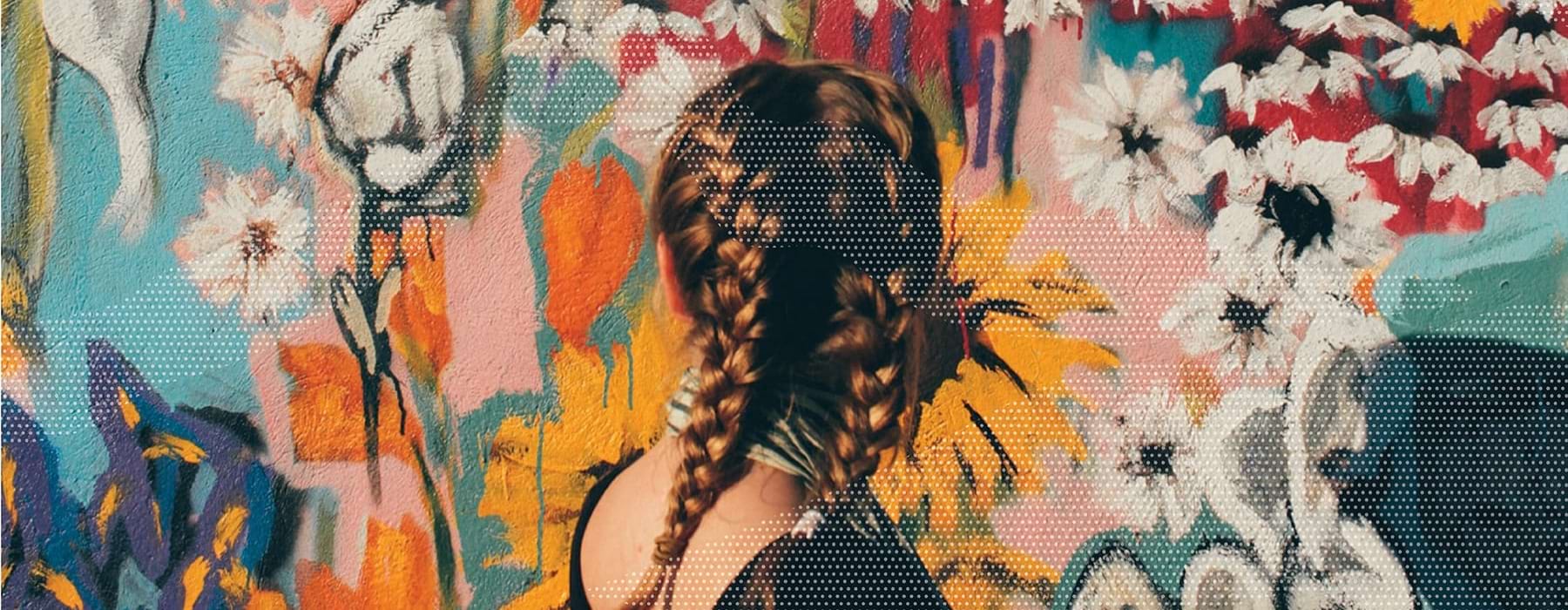 woman with two braids looks at an outdoor wall mural of colorful flowers