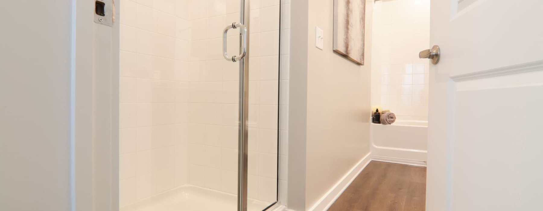 View from door looking into on-suite bathroom for large bedroom. A walk-in shower sits to the left. On the far wall a large soaking tub can be seen. Two framed pieces of art hang on the wall between the shower and the tub.