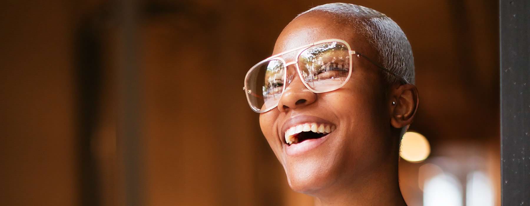 woman with large framed glasses laughs as she looks out her door